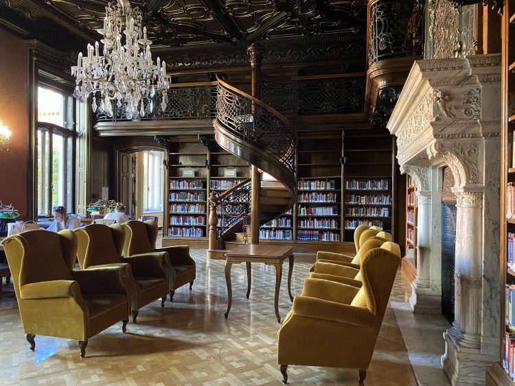 An oak-panelled library with a spiral staircase, chandelier and yellow armchairs